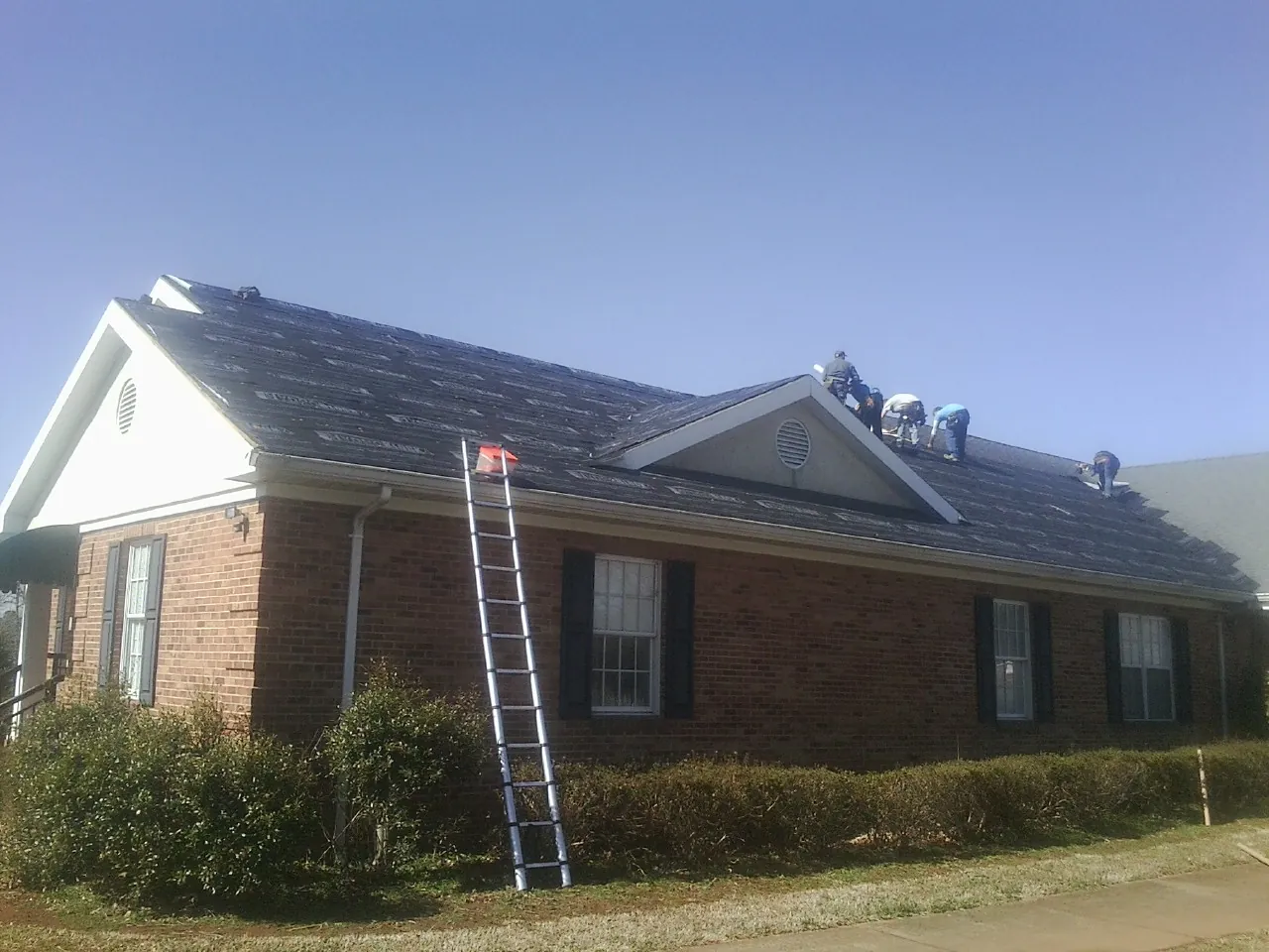Crew tearing shingles off a brick ranch roof with a ladder set — Metal Roof Repair work by our crew in Syracuse