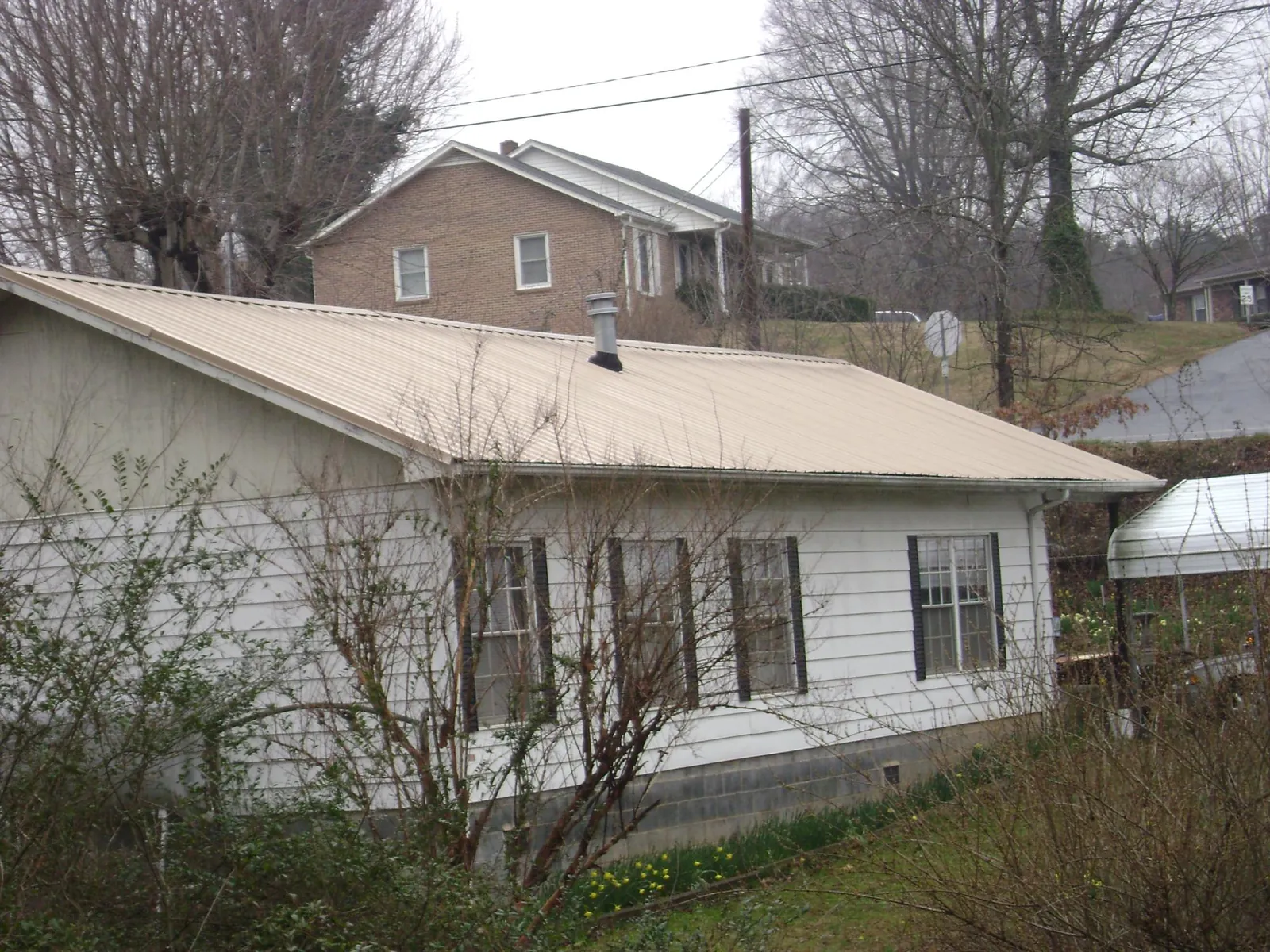 Tan metal roof on a white sided house set into a hillside — Commercial Roofing by Roofing Brothers in Syracuse